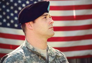 man-wearing-combat-hat-and-top-looking-up-near-flag-of-1202726
