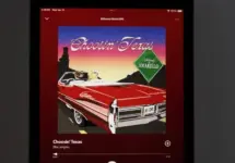 An Apple iPad displays the Spotify music streaming application^ which is playing the song "Choosin' Texas" by the artist Ella Langley