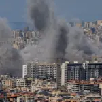 Multiple large plumes of thick grey smoke billow from residential apartment complexes following an explosion or missile strike in a crowded urban skyline. Jan 3 2021 in Iran