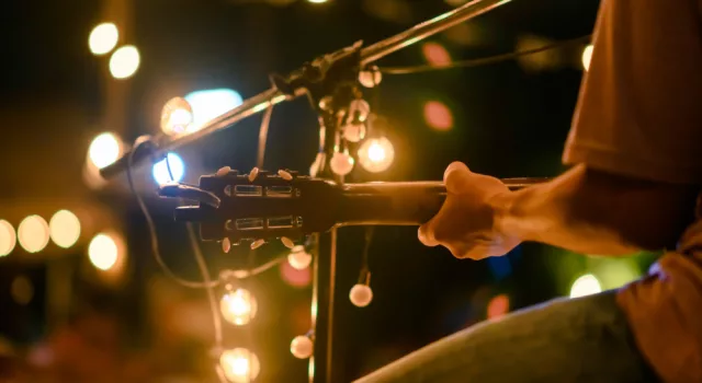 Rear view of the man sitting play acoustic guitar on the outdoor concert with a microphone stand in the front