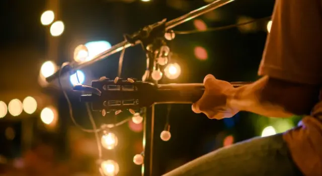 Rear view of the man sitting play acoustic guitar on the outdoor concert with a microphone stand in the front^ musical concept.