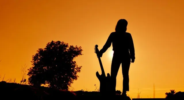 Silhouette Hipster woman with guitars in the meadow.