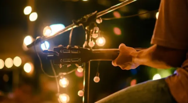Rear view of the man sitting play acoustic guitar on the outdoor concert with a microphone stand in the front^ musical concept.