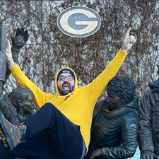 A handsome man does a Lambeau Leap. 