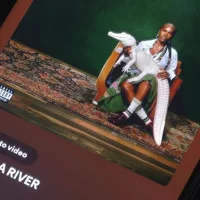 Album art of music artist Doechii from Spotify^ displayed on a phone screen on a dark surface^ playing song "DENIAL IS A RIVER"