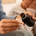 Mother giving cough syrup to her sick son in bed