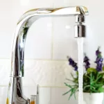 Open kitchen sink faucet flowing stream of water purified by domestic reverse osmosis with filters around. Front view. Horizontal composition.