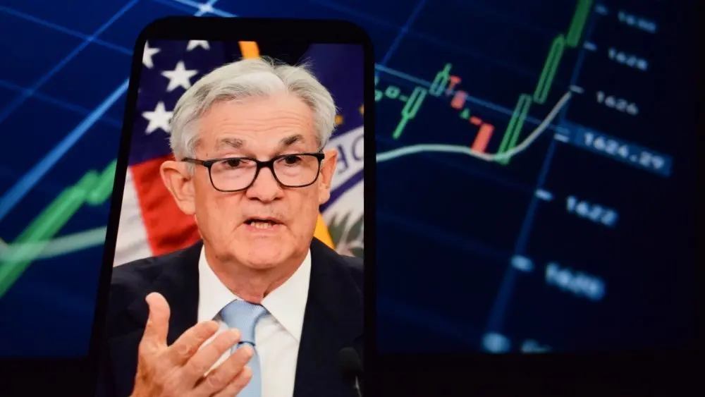 Federal Reserve (Fed) Chair Jerome Powell is visible. In the background^ an inflation rate chart is displayed.