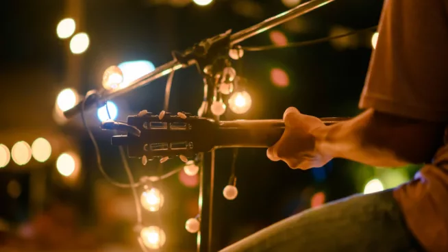 Rear view of the man sitting play acoustic guitar on the outdoor concert with a microphone stand in the front