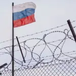 View of russian flag behind barbed wire against cloudy sky. Concept anti-Russian sanctions. A border post on the border of Russia.