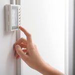 woman-adjusting-thermostat-on-white-wall-closeup-heating-syste