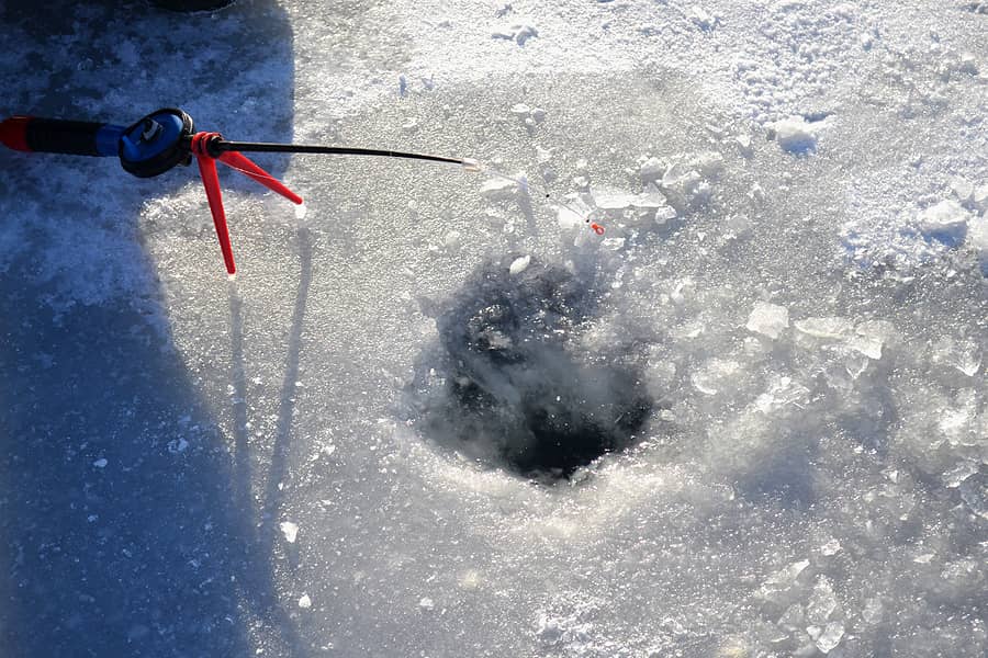 winter-ice-fishing-fisherman-sitting-near-ice-hole-and-holding