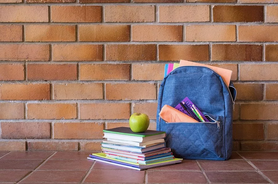 blue-backpack-with-school-supplies-against-brick-wall-full-scho