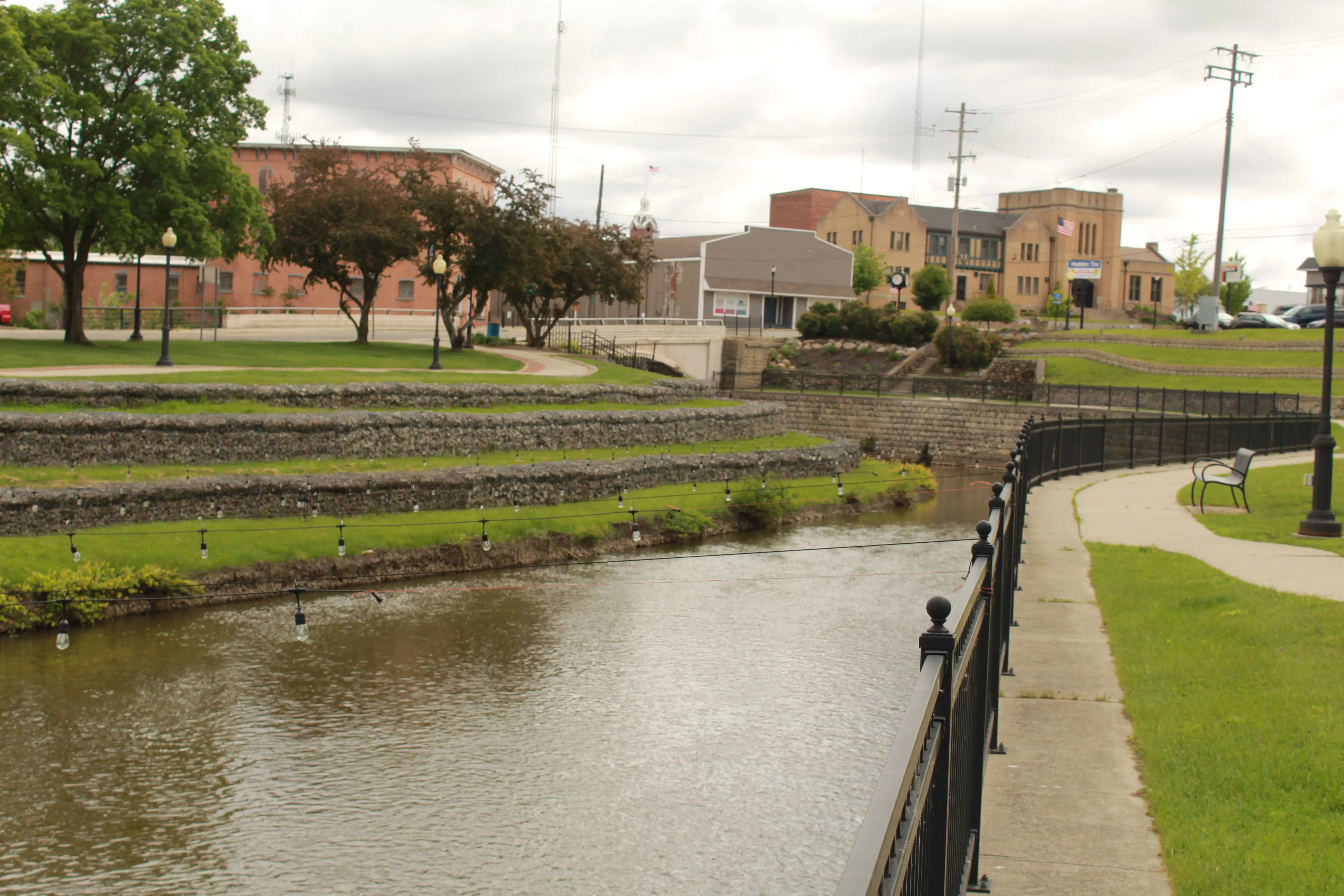 downtown-adrian-wlen-building-river-string-lights-terraced-grass-fenced-walkway-bench