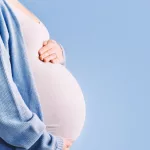 pregnant woman holding her belly in silhouette/ blue background.