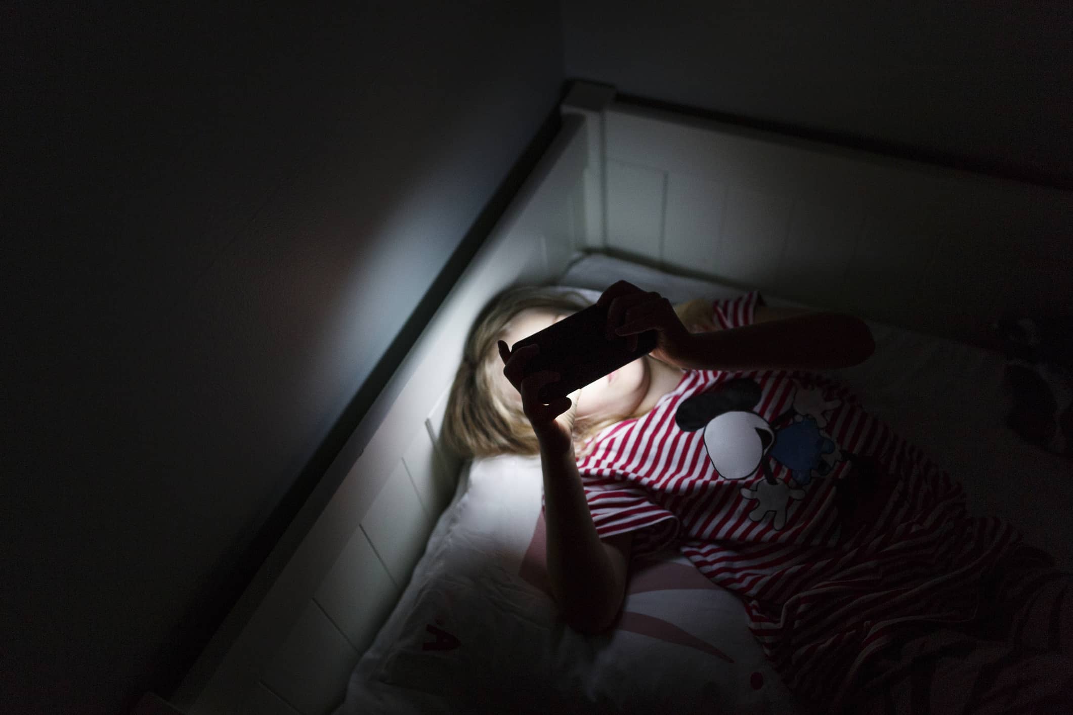 girl-using-smartphone-in-dark-room-while-lying-in-bed