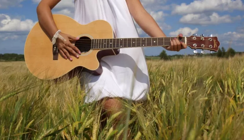 girl playing guitar in field over blue sky.