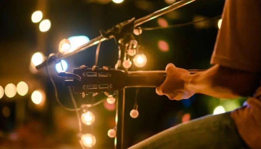 Rear view of the man sitting play acoustic guitar on the outdoor concert with a microphone stand in the front^ musical concept.