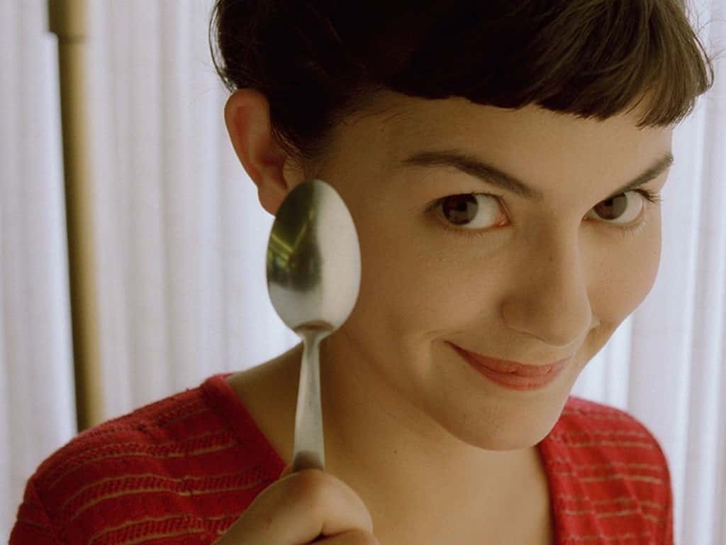 Audrey Tautou as Amélie Poulain looks directly at the camera as she holds a spoon next to her face