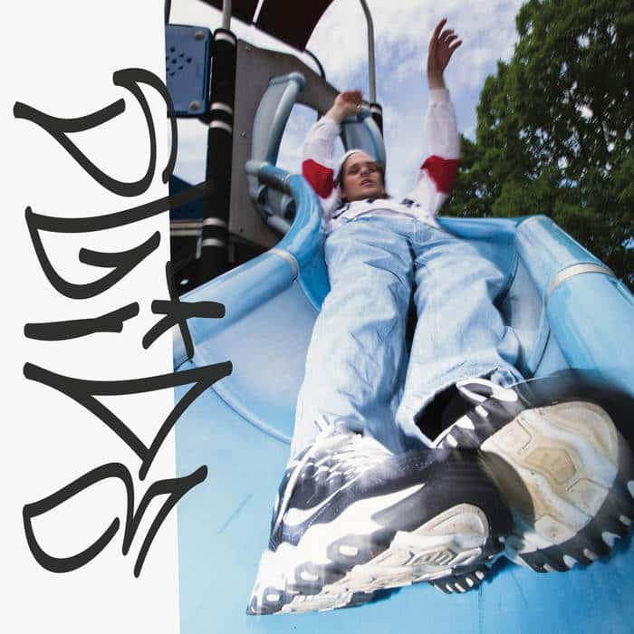 A man in blue jeans and chunky sneakers slides down a playground slide towards the camera
