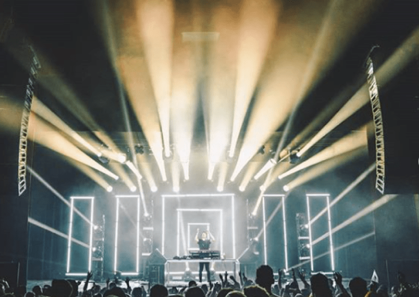 Matoma with his hands up as white beams of light explode from the stage.