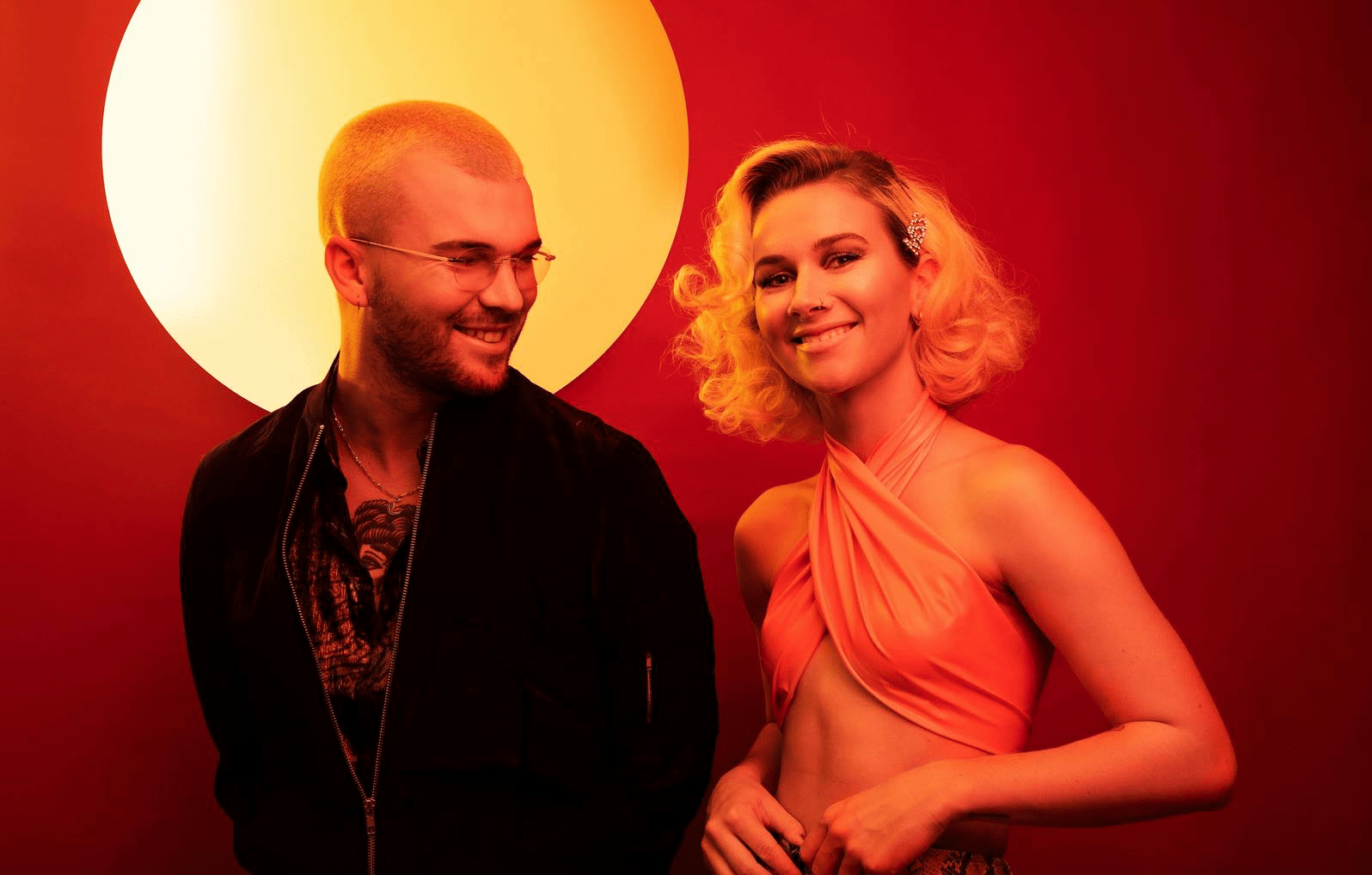 The duo, Broods, smiling and lit by orange hues.