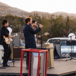 The members of Local Natives preform on an outdoor stage in the desert
