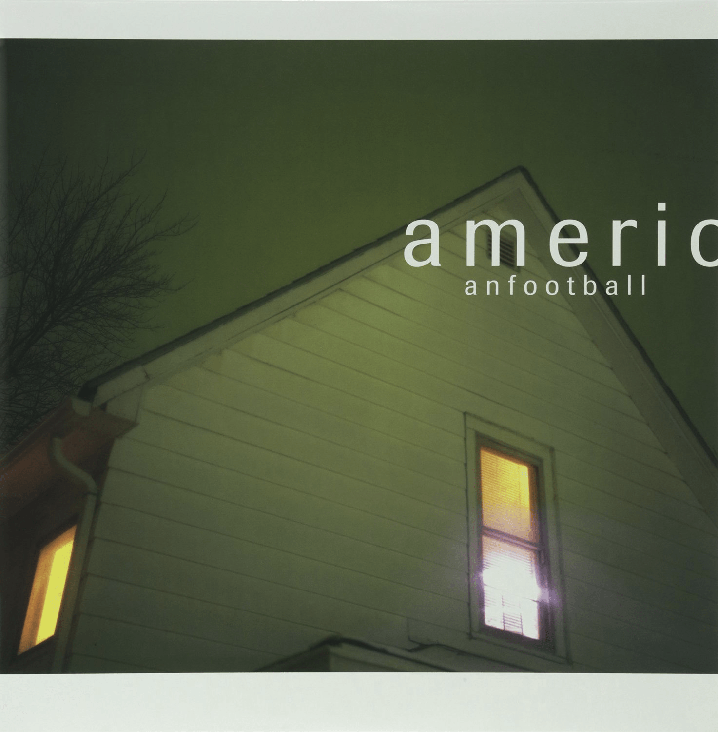 The album cover to American Football's first album. It features the roof of a house bathed in green light. Two windows are visible, with yellow light pouring from inside the home. The text "American Football" is written in the top right corner