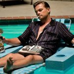 Leonardo DiCaprio is sitting in a floating lawn chair in a pool as he smokes a cigarette, listens to a tape player, and drinks from a large stein.