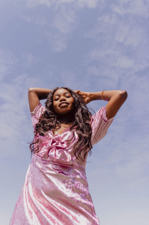 A female model poses in a pink dress, and a background of blue sky.