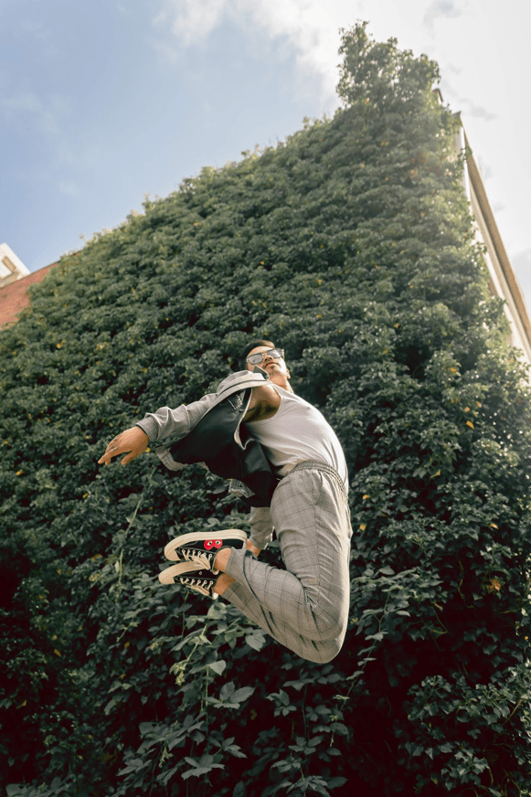 A male model is jumping in front of a wall of leaves