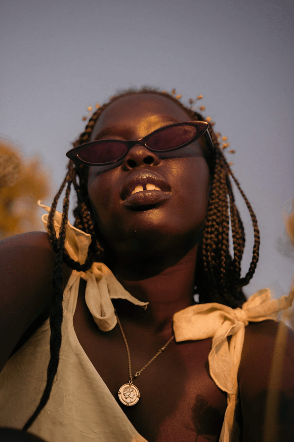 A headshot of a female model wearing a yellow dress and black sunglasses