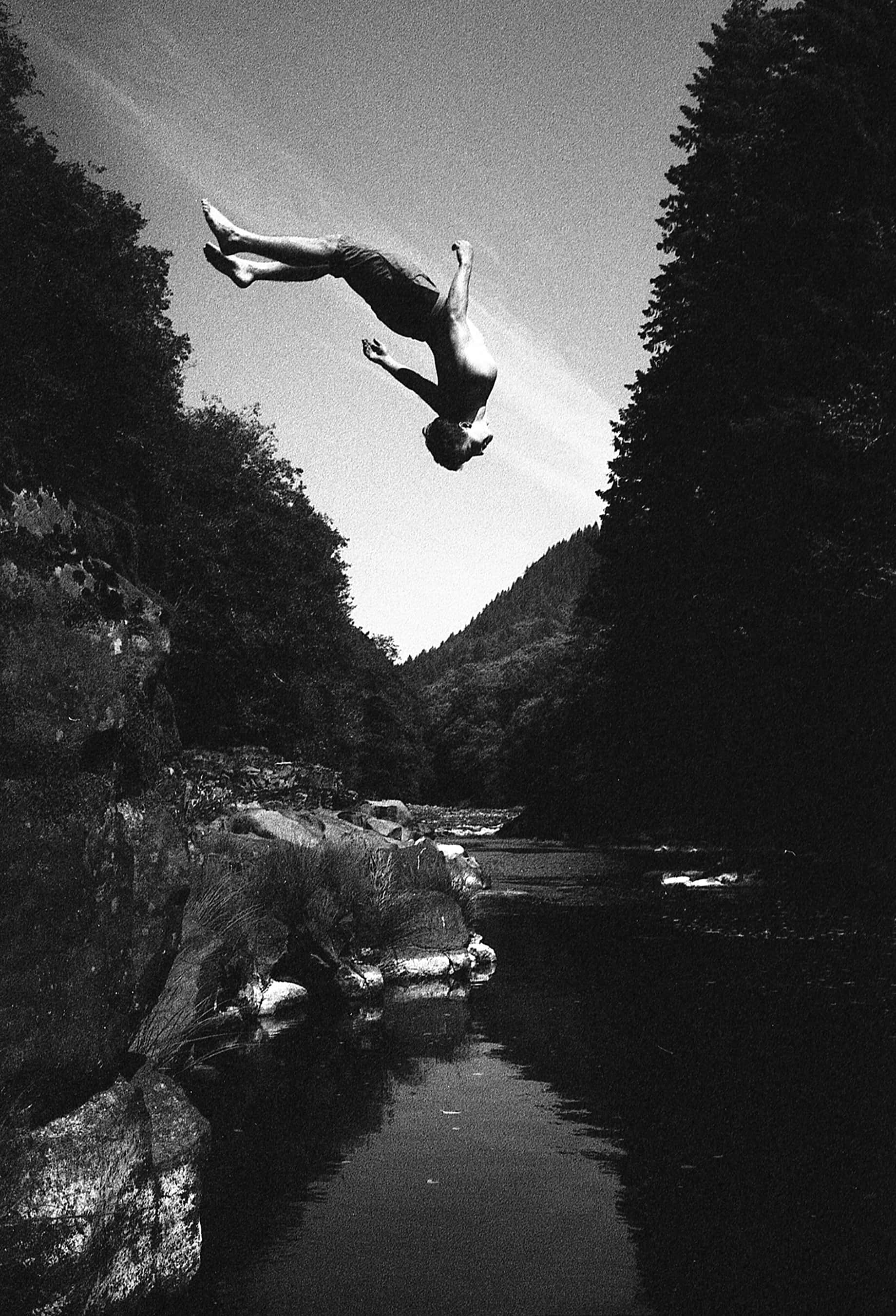 A man does a backflip into a pool of water, black and white photo.