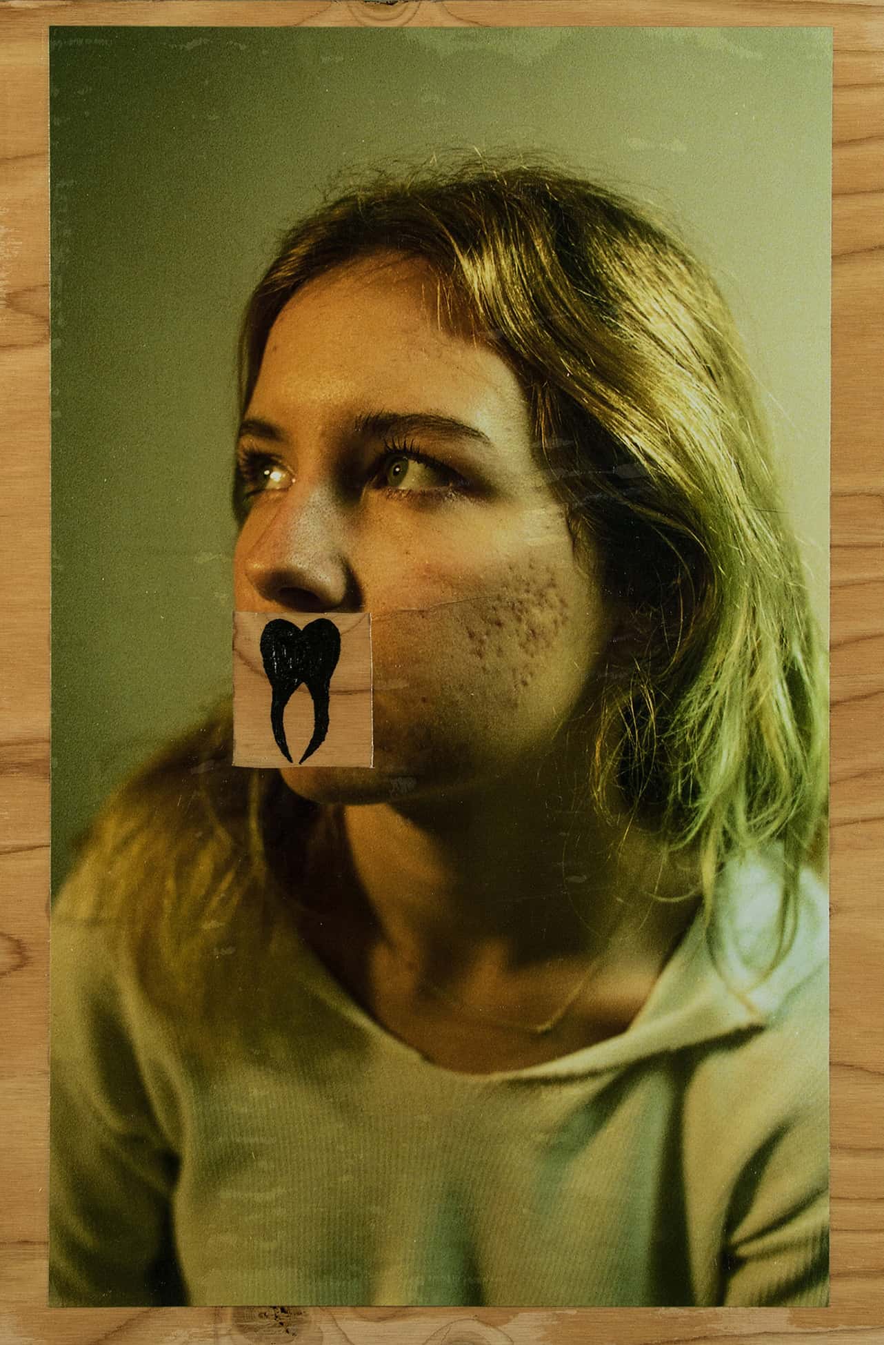 A photo of a girl looking forward with a tooth drawn over her mouth on a wooden background.