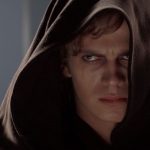 A close up of Anakin Skywalker (Hayden Christensen) with the hood of the Jedi robe he is wearing hiding most of his face. He looks angry and deeply troubled.