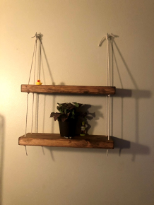 two dark wooden shelves hanging from a wall that are held together with beige rope. The same rope is tied on to two hooks. There is also a plant and a rubber duck on the shelves