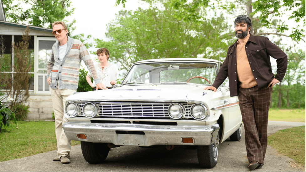 Paul Bettany, Sophia Lillis, and Peter Macdissi stand outside around a car in the film "Uncle Frank"