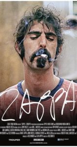 Movie poster of Frank Zappa smoking a cigarette. He is wearing a salmon colored shirt and "Zappa" is written over the image.
