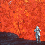A scientist stands beneath a towering eruption of bright red lava in a silver protective suit.