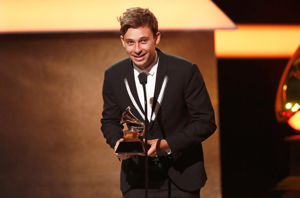 Streten shown on stage accepting his grammy award on stage wearing a suit and tie