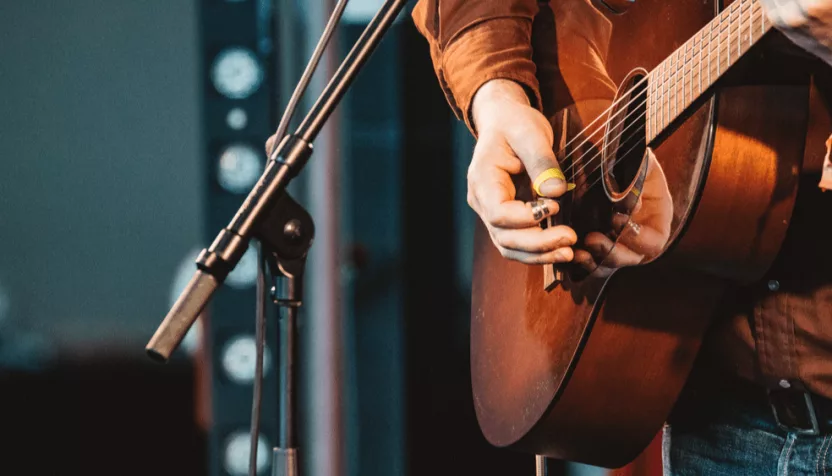 close up of hand of man playing guitar in concert on stage