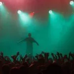 Rap singer performing on concert in music hall. Silhouette of rapper singing on stage in night club. Popuar hip hop music festival. Crowd of fans partying on dance floor