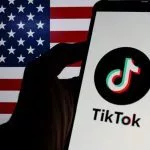 Photo illustration of TikTok logo displayed on a smartphone with American Flag in the background.