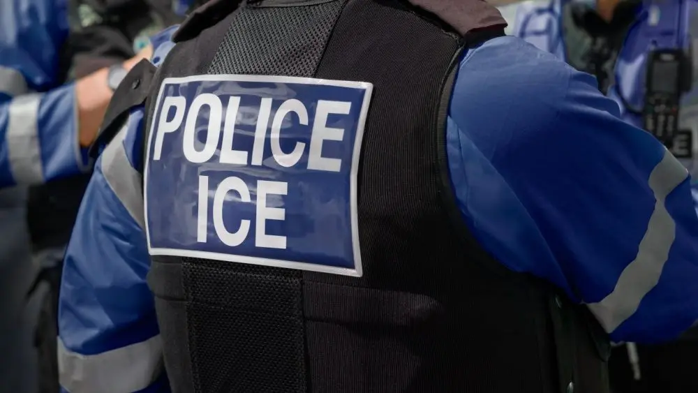 ICE police agent - Officer of Immigration and Customs Enforcement. Close-up of POLICE ICE marking on the back of a stab proof vest uniform worn by a trio of police officers at the scene of an incident