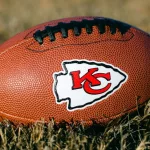 Kansas City Chiefs branded football laying on the grass^ with the arrowhead KC logo showing.