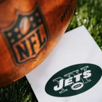 New York Jets logo on the ground and official NFL ball on green grass. Jets card^ edit space