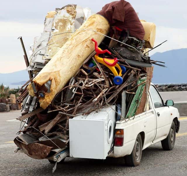 white-truck-driving-down-road-carrying-a-pile-of-rubbish