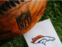 Denver Broncos NFL team Logo and American football ball on Green Grass.