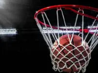Looking up at an orange basketball falling through the rim and a white nylon net. With the arena lights in the background.