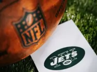 New York Jets logo on the ground and official NFL ball on green grass. Jets card^ edit space